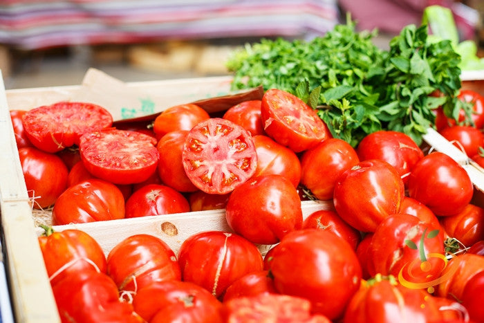 Fresh vibrant red VR Moscow tomatoes, whole and halved, displayed with green herbs in wooden crates